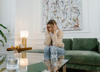 Kimerült nő kanapén ülve, fejét fogva, az empátiás kiégés és érzelmi túlterhelés illusztrációjaként